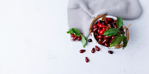 Cornelian cherries with green leaves in white bowl on light background with cloth