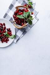 Cornelian cherries with leaves in ceramic bowl and on ribbed plate over checkered textile background