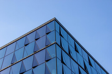 Modern architectural building with a striking glass facade featuring triangular patterns,...