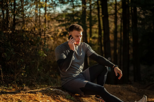 Male athlete taking a break during training in woods, using smartphone