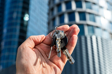 Keys to Success: Hand Holding Keys Against Futuristic Skyscraper. Symbolic image of a hand holding a bunch of keys with a modern glass skyscraper
