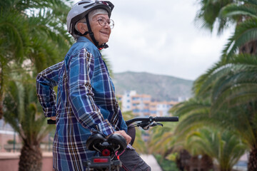 Smiling senior caucasian cyclist woman in leisure activity in urban park riding with electric bike...