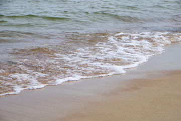 Wave splashing on sandy beach, clear Baltic sea water, foam, natural coastline. Bright outdoor scene, travel, summer, relaxation, peaceful nature.