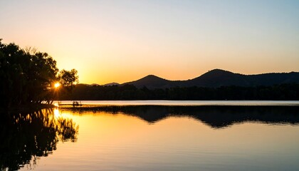 Sunrise over a serene lake, silhouetted trees and mountains