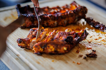 Succulent BBQ ribs are being enjoyed and cut apart on a wooden cutting board with a fork, perfect for summer cookouts, family dinners, or food blog inspiration