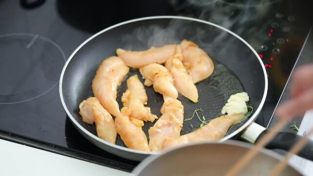 Woman frying chicken fillet in a pan at home kitchen, preparing a simple homemade meal.