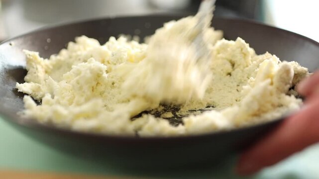 Close-up of female hands mixing fresh cottage cheese in a bowl with a spoon. Rustic homemade dairy preparation in a cozy kitchen with organic ingredients
