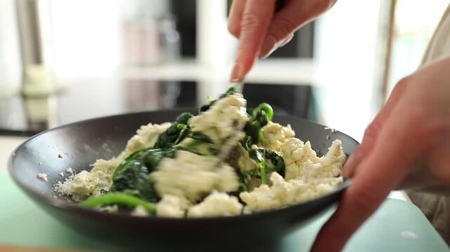 Close-up of female hands mixing fresh cottage cheese in a bowl with a spoon. Rustic homemade dairy preparation in a cozy kitchen with organic ingredients