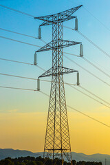 Silhouette of a black electricity transmission tower with power lines stretching across the sky at sunset. Vertical photo