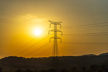Silhouette of a black electricity transmission tower with power lines stretching across the sky at sunset