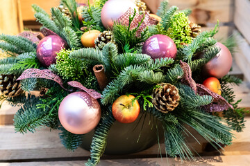 Christmas arrangement of fir and pine branches with pine cones, pink Christmas tree balls, apples and cinnamon sticks, selective focus