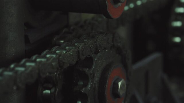 Close up of a dirty, oily roller chain turning on a sprocket gear as part of a large industrial machine, illustrating mechanical power transmission and industrial manufacturing concepts