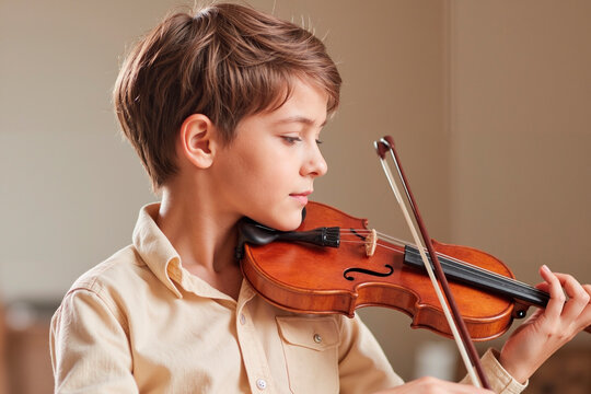 Caucasian boy child playing violin with focused expression, holding instrument under chin and drawing bow across strings, practicing music in indoor setting, side profile visible