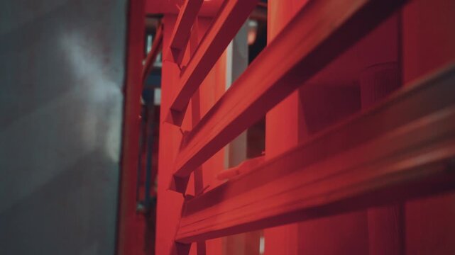 Industrial robotic arm spraying red paint on metal profiles hanging on a conveyor line inside a factory spray booth, providing a smooth and durable powder coated finish for manufacturing