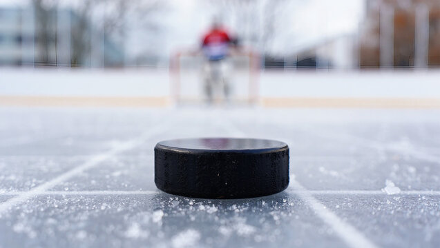 Black hockey puck on ice rink with blurred player and net sport - Powered by Adobe