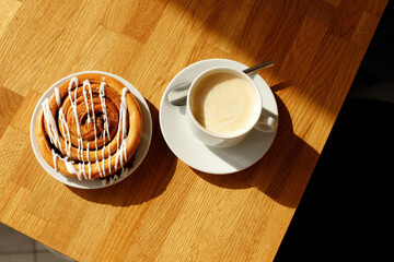 white cup of coffee on the saucer and freshly baked bun on hte wooden table
