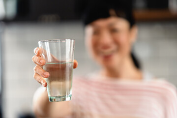 Smiling Japanese woman offering a glass of water in a modern kitchen, symbolizing hydration, kindness, and healthy living at home