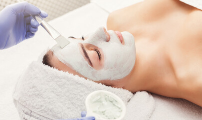 A woman enjoys a soothing facial treatment with a calming mask applied to her skin. She lies comfortably on a treatment bed in a serene spa environment, promoting relaxation and rejuvenation.