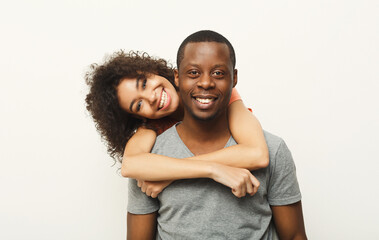 A man and woman are smiling brightly as the woman embraces the man from behind. They display happiness and connection, enjoying a light-hearted moment together.