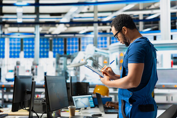 Male specialist in solar panel power plant reviews photovoltaic system performance on files. Engineer analyzing production line on clipboard to optimize efficiency, troubleshooting.