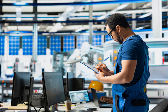 Male specialist in solar panel power plant reviews photovoltaic system performance on files. Engineer analyzing production line on clipboard to optimize efficiency, troubleshooting.