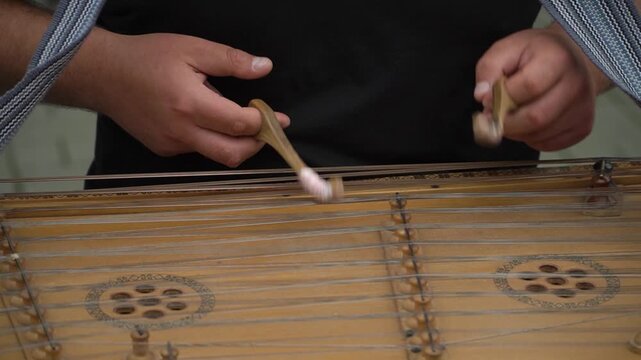 A musician in a black T-shirt professionally and masterfully plays the cymbals with sticks, quickly tapping the strings, a traditional folk ancient musical instrument