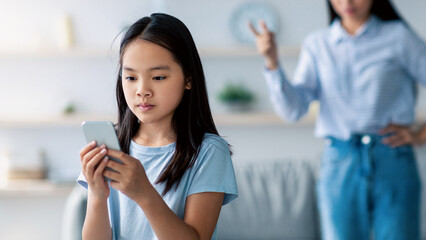 Asian mother and daughter quarreling because of overuse the smartphone, girl not paying attention...