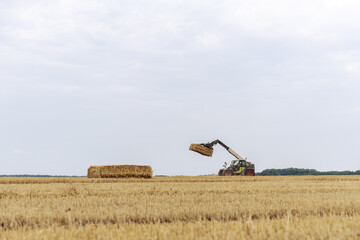 A Rural Scene with a Tractor Lifting Straw Bales in a Golden Field Under a Cloudy Sky, Capturing the Essence of Agriculture and Hard Work in Nature's Bounty