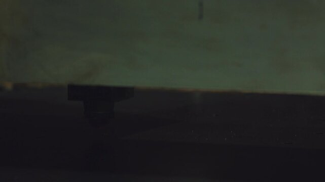 Close up shot of a cnc laser cutting machine head precisely engraving a metal sheet, creating bright orange sparks and smoke in a dimly lit industrial factory workshop during production