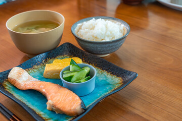 Japanese breakfast with grilled salmon, tamagoyaki, cucumber side dish, rice and miso soup
