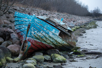 Abandoned blue and red wooden boat, weathered by time, rests on a rocky shore.