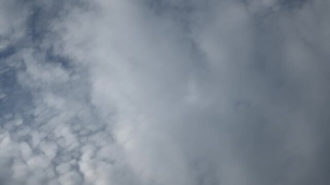 Looking up into a blue sky at white and gray clouds moving rapidly in a time lapse. The clouds close in to fill the sky. Sky only in the clip.
