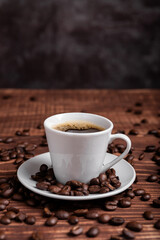 A cup of dark roasted coffee on a white saucer, surrounded by coffee beans on a brown wooden surface