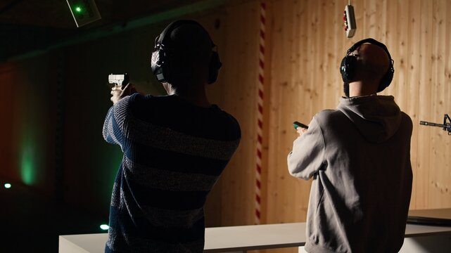 Man holds pistol, enjoying recreational shooting experience in firing range next to instructor reloading weapons. Employee loading firearms for shooting range company customers, camera A