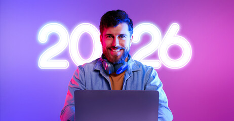 Caucasian programmer sits at a desk with a laptop in a vibrant neon purple and blue studio, focused on his work. He smiles at the camera, embodying the spirit of the online professional world.