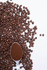 A spoonful of coffee beans is spread out on a white background. Concept of warmth and comfort, as coffee is often associated with relaxation and socializing. The spoon