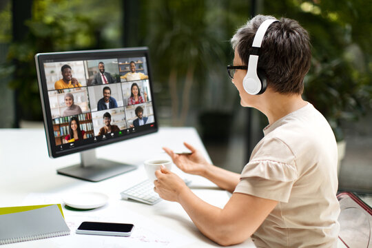 Middle aged woman remote employee have online meeting with international colleagues, working at coworking space, using computer pc and wireless headphones. Telecommunication, remote job