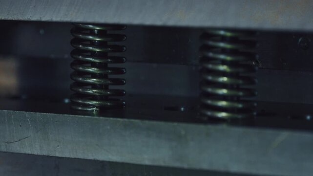 Close up view of an industrial press machine operating, with metal springs compressing and decompressing as the heavy plates move up and down during a manufacturing process in a factory
