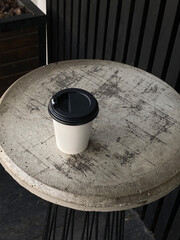 Paper cup of coffee with black lid sits on vintage table in street cafe. Concept is one of takeaway coffee, minimalism, and urban everyday life. Copy space. 