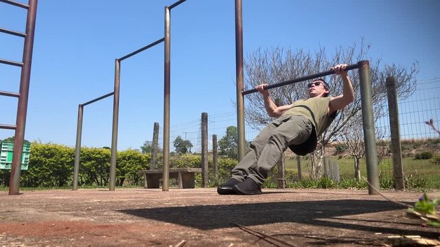 homem faz exerc&iacute;cios f&iacute;sicos em barra ao ar livre 