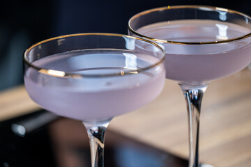 Elegant cocktails in crystal glasses with golden rims, showcasing a soft purple hue, placed on a wooden table, creating a sophisticated and inviting atmosphere for gatherings