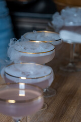 Elegant cocktails with dry ice creating a foggy aura, arranged on a wooden surface, enhancing the mysterious atmosphere for a vibrant party show concept