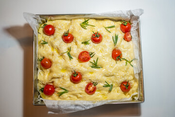 Focaccia bread topped with cherry tomatoes and fresh rosemary, showcasing a soft and fluffy dough, baked to perfection in a rectangular pan, representing culinary tradition and deliciousness