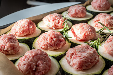 Raw meatballs placed on sliced zucchini with fresh rosemary sprigs, ready for baking in a modern kitchen, showcasing healthy meal preparation and culinary creativity