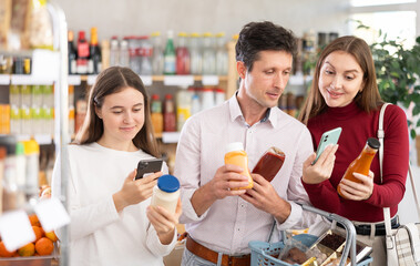 Couple adult man and young woman with teenage daughter scanning qr code for sauces in grocery store