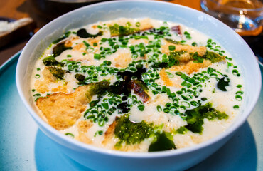 Overhead view of Norwegian fish soup, creamy broth served in a white bowl with fish fillet, bread, and fresh scallions from a Norway local restaurant.