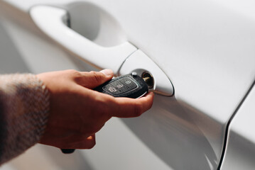 black car keys in woman hand, close-up view, white car in background, opening or closing car with signalization or alarm system, car theft, carjacking, car safety concept, selective focus