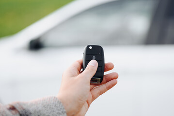 black car keys in woman hand, close-up view, white car in background, opening or closing car with signalization or alarm system, car theft, carjacking, car safety concept, selective focus