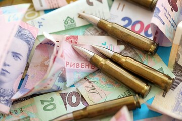 Many rifle bullets lies on lots of ukrainian money bills close up