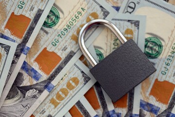 Small black padlock lies on big amount of new hundred US dollar bills